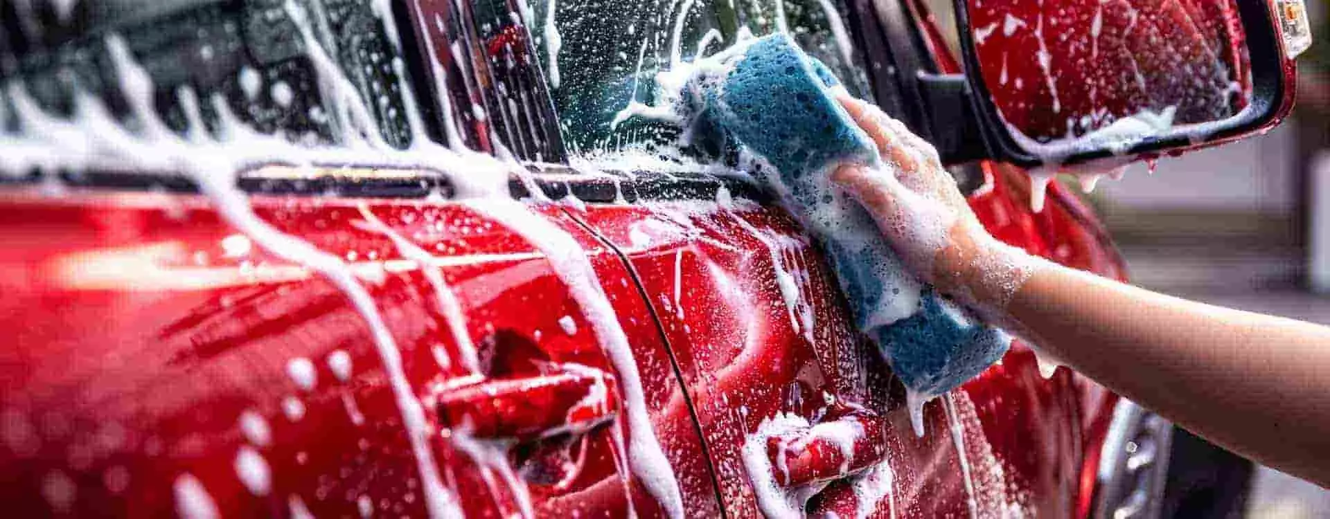 Kézi autómosás aktív habbal és kíméletes szivaccsal egy piros személyautón Örkényben